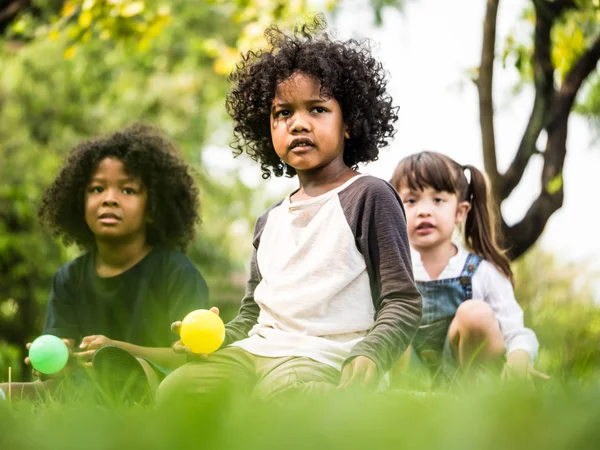 Niños jugando a las bolas juntos. Grupo de niños sentados en la hierba en un parque . — Foto de Stock