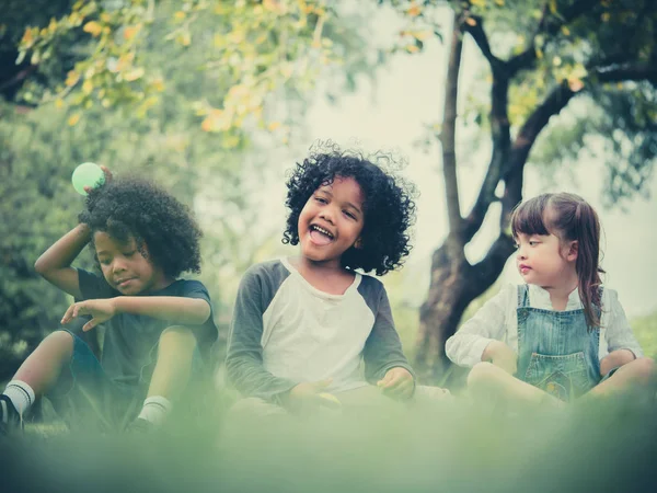 Niños jugando a las bolas juntos. Grupo de niños sentados en la hierba en un parque . — Foto de Stock