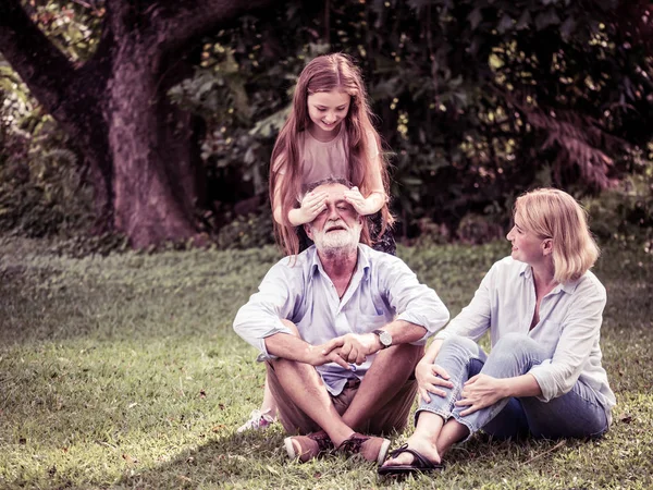 Família feliz se divertindo juntos no jardim. Pai, mãe e filha sentados na grama em um parque . — Fotografia de Stock