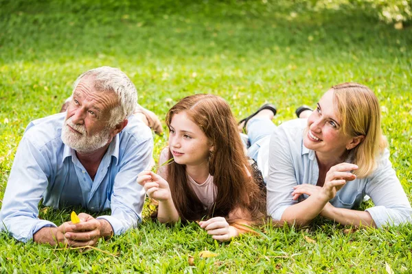 Família feliz se divertindo juntos no jardim. Pai, mãe e filha sentados na grama em um parque . — Fotografia de Stock