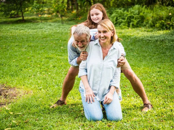 Família feliz se divertindo juntos no jardim. Pai, mãe e filha sentados na grama em um parque . — Fotografia de Stock