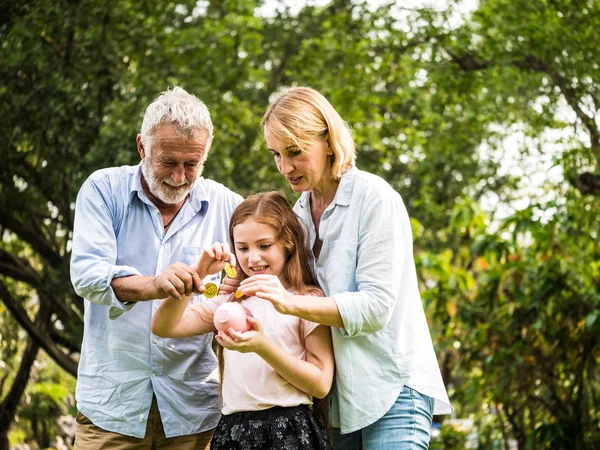 Pai, mãe e filha segurando um banco porquinho e moedas em um parque. Família e economia para o conceito futuro . — Fotografia de Stock