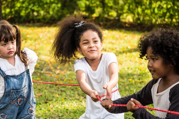 Маленькая девочка играет в перетягивание каната со своими друзьями в парке — стоковое фото