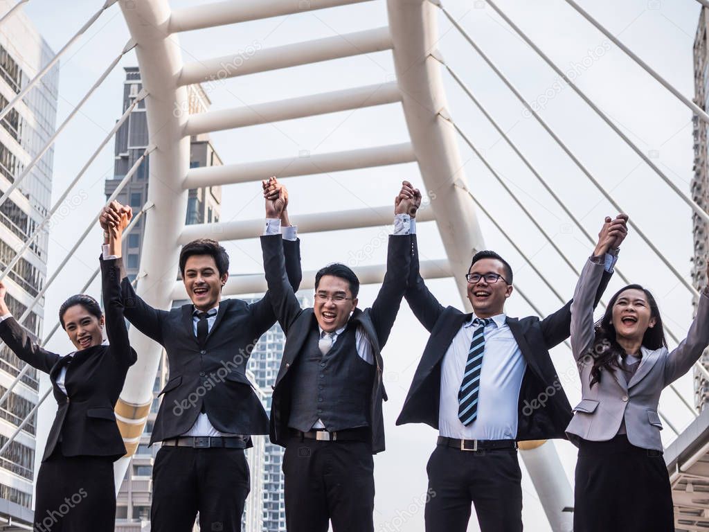 Successful Asian business team celebrating their triumph with arms up. Teamwork and success concept