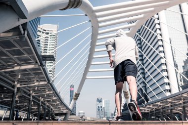 Arkadan görünüş atletik gencin şehir köprüsü üzerinde Bangkok kentsel sahne arka plan ile sabah koşan sportif adam koşu