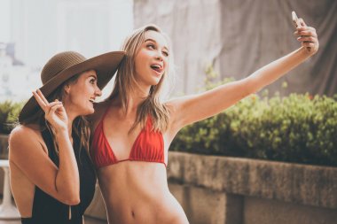 İki güzel kız eğleniyor yüzme havuzunda akıllı telefon kamera ile selfie fotoğraf çekme