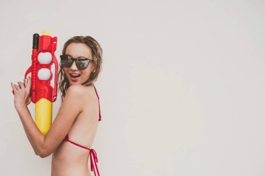 Kırmızı bikinili çekici bir kadın beyaz arka planda su tabancası tutuyor.