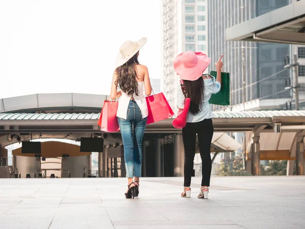 Vista posterior de las mujeres jóvenes con bolsas de compras disfrutando de las compras, chicas asiáticas se están divirtiendo con sus compras en la ciudad. Concepto de consumo y estilo de vida —  Fotos de Stock