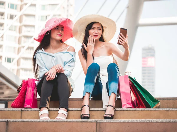 Dos hermosas mujeres jóvenes sentadas en las escaleras y haciendo autorretrato por teléfono inteligente después de disfrutar en las compras —  Fotos de Stock