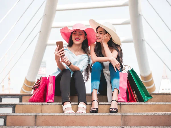 Dos hermosas mujeres jóvenes sentadas en las escaleras y haciendo autorretrato por teléfono inteligente después de disfrutar en las compras —  Fotos de Stock