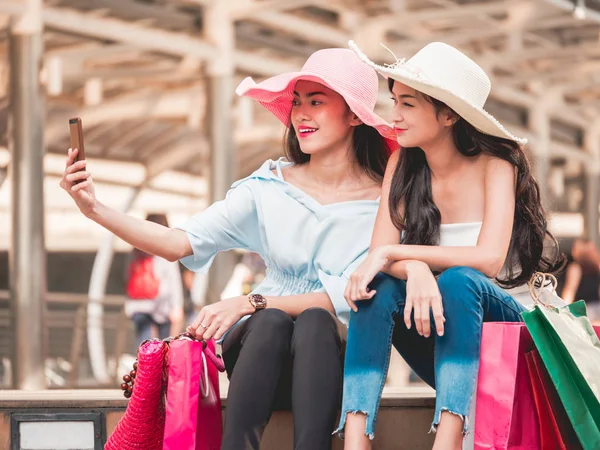 Dos hermosas mujeres jóvenes sentadas en las escaleras y haciendo autorretrato por teléfono inteligente después de disfrutar en las compras — Foto de Stock