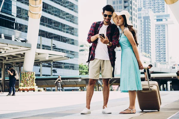 Couple Asian travelers are walking on city street and looking at interesting places to travel from smart phone. Vacation and technology Concept — Stock Photo, Image