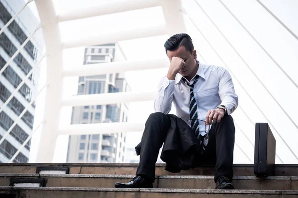 Frustrierter asiatischer junger Geschäftsmann sitzt vor dem Bürogebäude. — Stockfoto