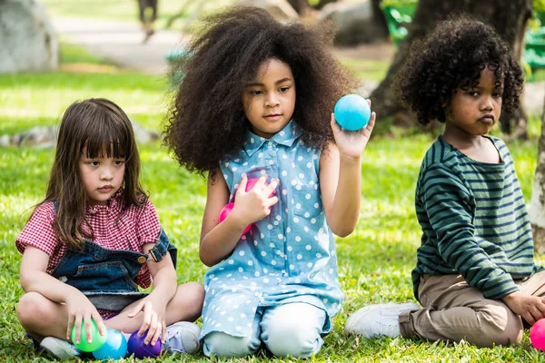 Les enfants jouent aux balles ensemble. Groupe d'enfants assis sur l'herbe dans un parc . — Photo