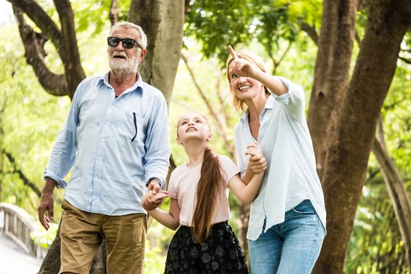 Família feliz se divertindo juntos no jardim. Pai, mãe e filha de mãos dadas e a caminhar num parque. Conceito de estilo de vida — Fotografia de Stock