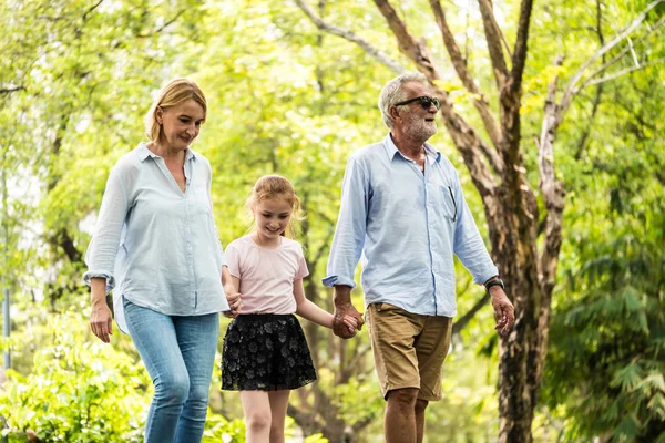 Família feliz se divertindo juntos no jardim. Pai, mãe e filha de mãos dadas e a caminhar num parque. Conceito de estilo de vida — Fotografia de Stock