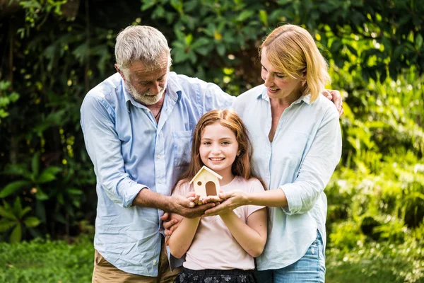 Pai, mãe e filha segurando um modelo de casa em um parque. Conceito de família casa . — Fotografia de Stock