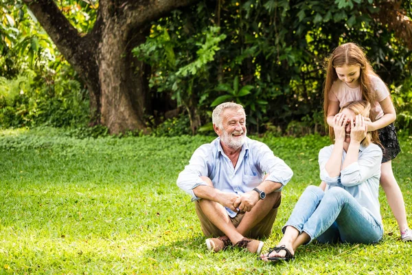 Família feliz se divertindo juntos no jardim. Pai, mãe e filha sentados na grama em um parque . — Fotografia de Stock