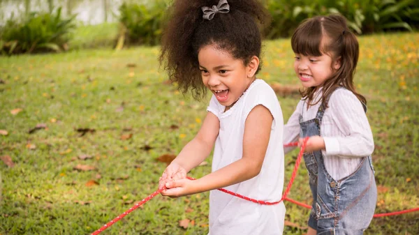 Una niña jugando a tirar de la guerra con sus amigos en un parque —  Fotos de Stock