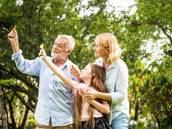 Pai, mãe e filha segurando um banco porquinho e moedas em um parque. Família e economia para o conceito futuro . — Fotografia de Stock