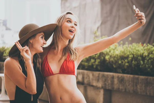 Dos hermosas chicas se divierten tomando foto selfie con la cámara del teléfono inteligente en la piscina — Foto de Stock