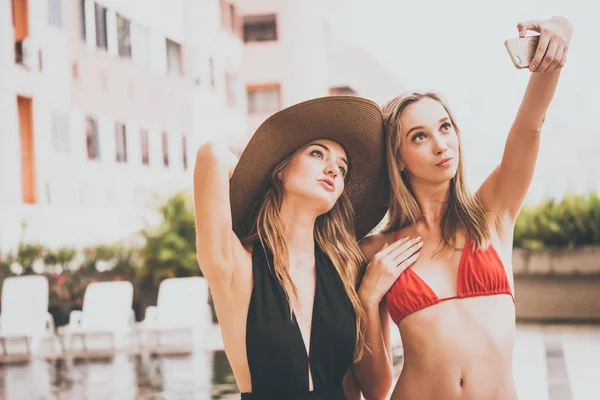 Dos hermosas chicas se divierten tomando foto selfie con la cámara del teléfono inteligente en la piscina —  Fotos de Stock
