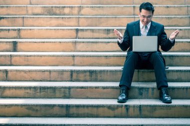 Mutlu Asya iş adamı şehir merdivenlerde otururken dizüstü bilgisayarda çalışıyor. Kopya alanı