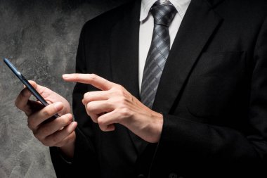 Bir akıllı telefon kullanarak gri grunge arka plan üzerinde siyah elbiseli adam yakın çekim