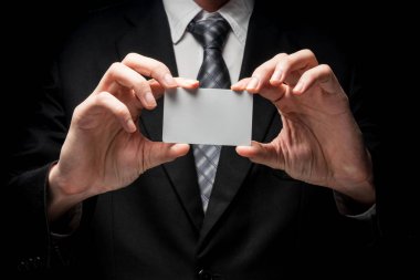 Kartvizit tutarak siyah arka plan üzerine siyah elbiseli adam yakın çekim