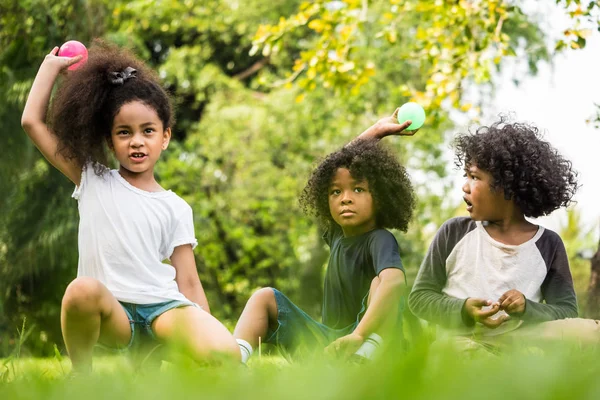 Barn som leker bollar tillsammans. Grupp av barn som sitter på gräset i en park. — Stockfoto