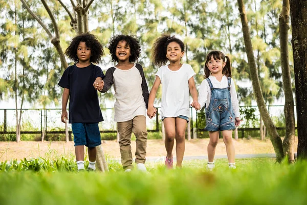 Grupo de niños divirtiéndose jugando juntos. Niños tomados de la mano y caminando en un parque . —  Fotos de Stock