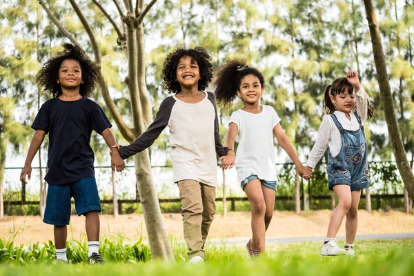 Grupo de niños divirtiéndose jugando juntos. Niños tomados de la mano y caminando en un parque . —  Fotos de Stock