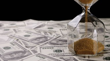 Kahverengi kum banknotların üzerine açık kum saati döküyor.