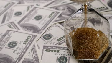 Kahverengi kum banknotların üzerine açık kum saati döküyor.