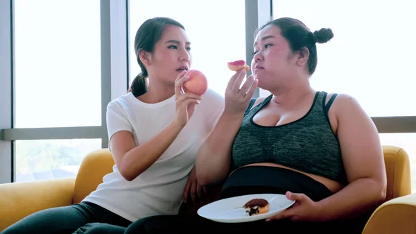 Young woman suggesting chubby woman to eat apple in the room.