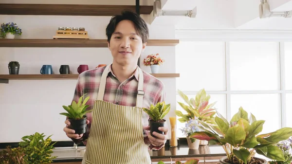 Young gardener man holding flowerpot in the room.