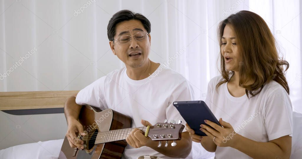 Happy asian lover playing guitar and singing songs together in a room.