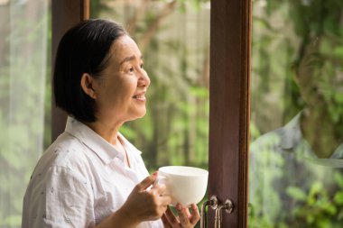 Asyalı bir kadın elinde bir fincan çayla dışarı bakıyor..