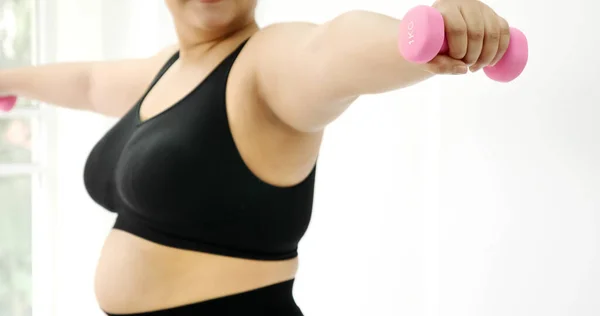 Chubby woman doing exercise by dumbbell in a room.