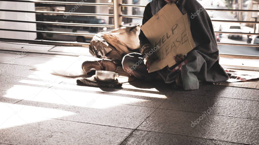 Homeless man sitting on outdoor floor.