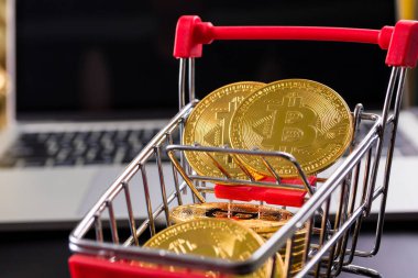 Bilgisayar geçmişi olan küçük bir alışveriş arabasında bitcoin sembollü altın paralar..