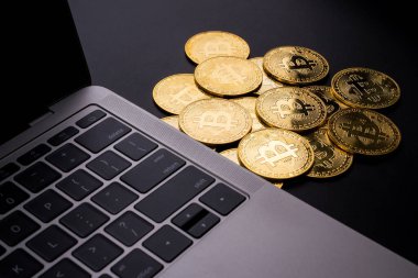 Siyah zemin üzerinde bitcoin sembolü olan bilgisayar ve altın sikkeler.