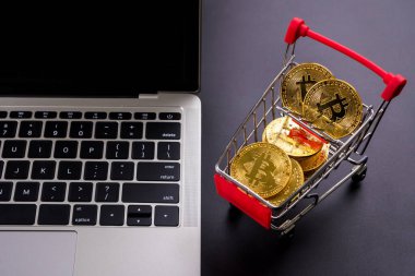 Üzerinde bitcoin sembolü olan altın paralar küçük bir alışveriş arabası ve bir bilgisayar..