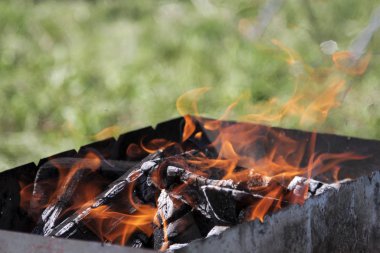 Soyut arkaplan. Bulanık yeşil çimlerin arkasındaki barbekü partisindeki şenlik ateşi barbekü sezonunun açılışını sembolize eder. Boşluğu kopyala.