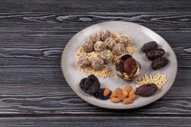 Enerji topları, tatlılar ev yapımı. Hurmalardan, kayısılardan, bademlerden, çam fıstıklarından ve ballı eriklerden yapılmış. Malzemeler gri kıvrımlı bir tabakta yatıyor. Koyu tahta arkaplan, boşluğu kopyala.