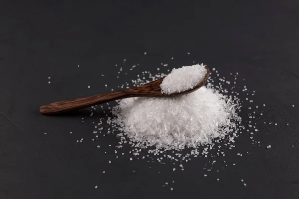 Monosodium glutamate (Msg) in a wooden spoon on a dark background. Food supplement E621. Taste seasoning to enhance the food experience. The additive is used in the food industry.