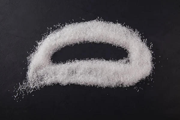 Food additive E621. Powdered crystals of sodium glutamate (Msg) are scattered on a dark background. The shape of the composition is similar to a sad smiley or a human brain. Top view, place for text.