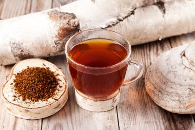 Chaga çayı - güçlü bir antioksidan, bağışıklık sistemini güçlendirir, detoks kalitesine sahiptir, sindirimi artırır. Masada huş ağacından yapılmış bir mantarın yanında bir bardak şifalı içecek var..