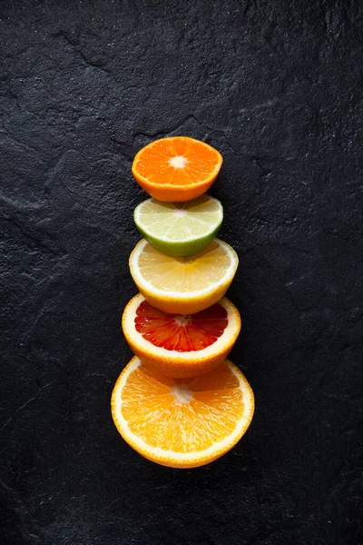 Fresh ripe citrus fruits cut in half. Lemon, lime, red orange and mandarin on a dark stone background. Top view with copy space.