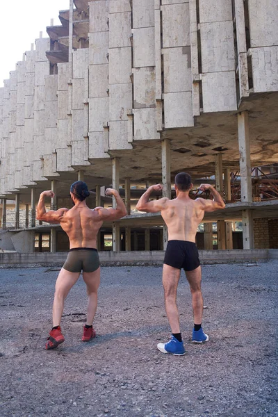 the two young muscular mans doing bodibuilding exercises in the city, two muscular young mans, athletic young mans in the park